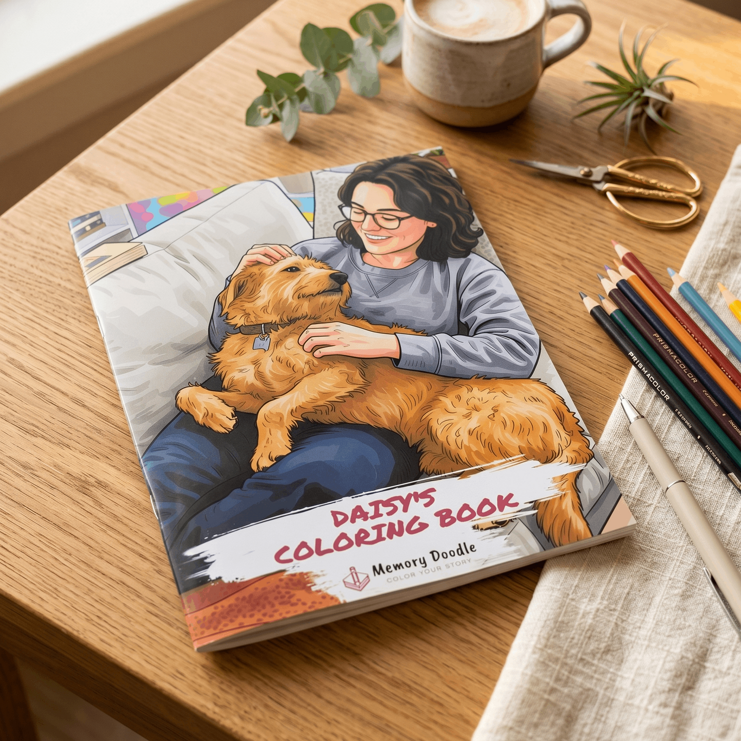 A custom coloring book titled 'Daisy's Coloring Book' by Memory Doodle lies on a wooden table next to a cup of coffee, scissors, colored pencils, and small green leaves. The cover features a colorful illustration of a woman hugging a golden dog.